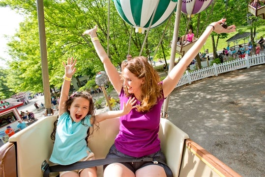 A mother and daughter raising hands while they soar above the trees on a gondola shaped like hot air balloons with the Balloon Race ride at Idlewood.