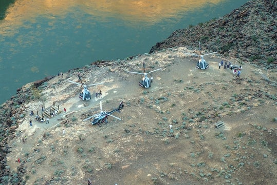 An aerial view of the Colorado River and picnic benches with tourist with four helicopters parked near them.