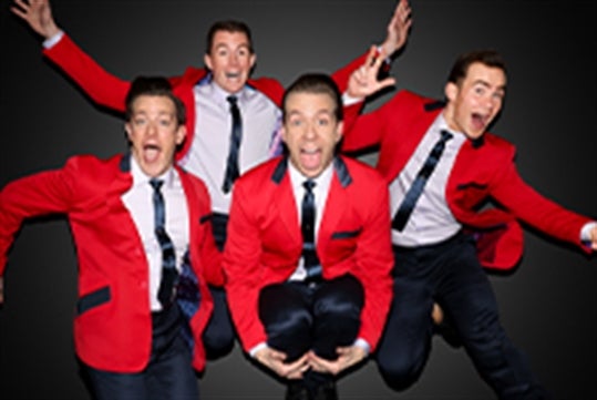 The Jersey Boys dressed in red suits and ties, all smiling and jumping in the air.