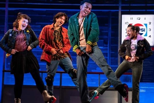 A four actors on stage dancing while wearing ice skates with their hands in their belt loops with a Pepsi clock behind them.