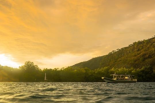 A super-raft floating in the ocean with a bright yellow cloudy sunset overhead and a lush island in the background.