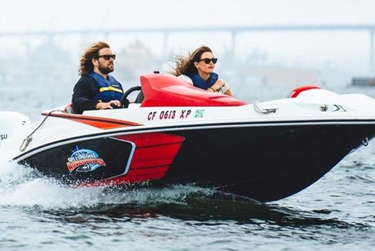 A man and woman in a white, red and black speed boat with the wind blowing their hair back on the Land and Sea: GoCar Tour + Speed Boat Adventure.