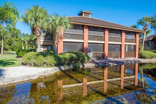 A small pond with clear water next to Legacy Vacation Resorts - Palm Coast with small palm trees and shrubs in the landscaping.