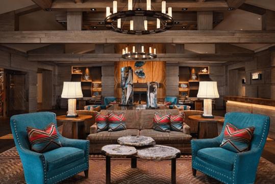 A western decorated lobby with a sitting area with a couch, coffee table, and two chairs with lots of leather and wood with blue and red accents