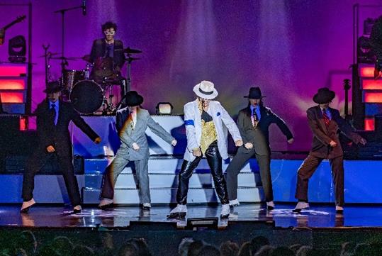 Michael Knight in a white Michael Jackson costume and the MJ the Illusion cast on stage dancing with a band behind them.