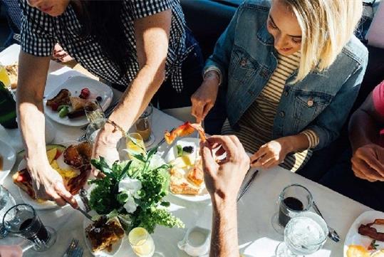 People gathered around a full brunch table helping themselves to what they want on the Marina del Rey Brunch Cruise.