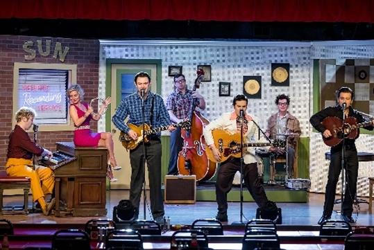 The cast of the Million Dollar Quartet on a 50s themed stage singing and playing various instruments.
