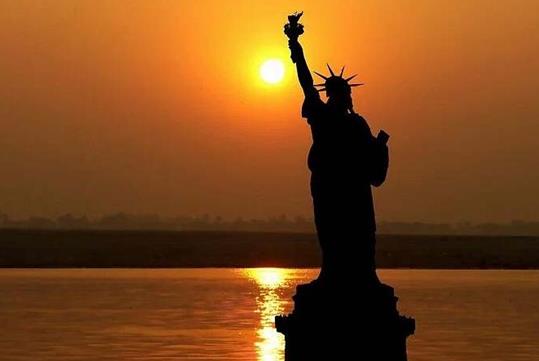 The silhouette of the Statue of Liberty with a bright orange sun setting behind it on the NYC Skyline Sunset Cruise.