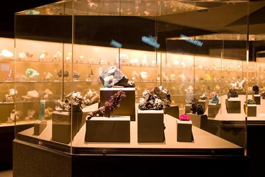 Several different gemstones elevated at different levels inside a glass display box with other boxes in the background.