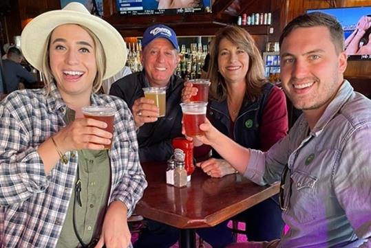 A group of adults sitting at a table holding their drinks up and smiling on the New Orleans Irish Channel Pub Crawl in New Orleans, Louisiana.