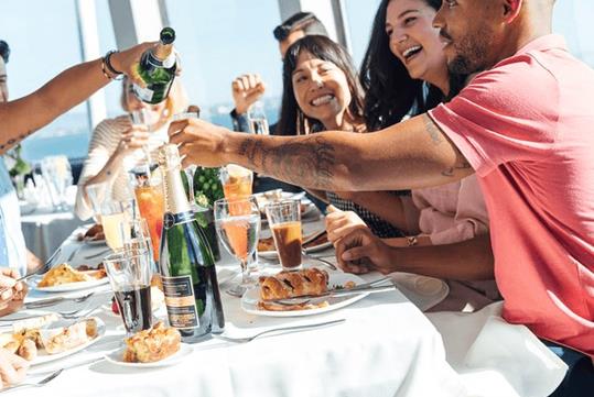 A group of friends laughing and smiling while having brunch on a bright and sunny day on the New York Brunch Cruise Pier 15.