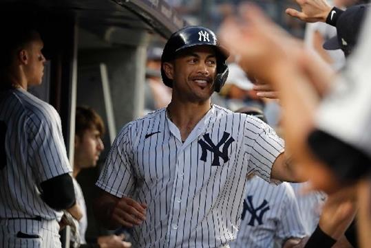 A Yankees player walking through a full dugout high-fiving other players and smiling.
