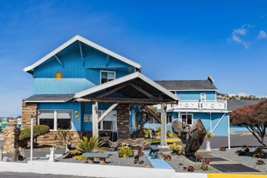 The Oceanside Inn & Suites exterior with blue siding with white accents and lots of landscaping on a sunny day.