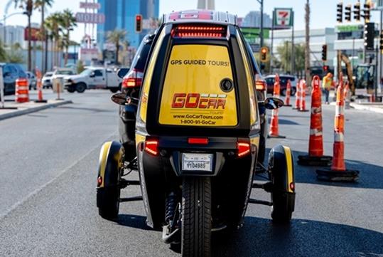 The back of a yellow GoCar stopped in traffic with the company's contact info and logo on the back panel in Las Vegas.