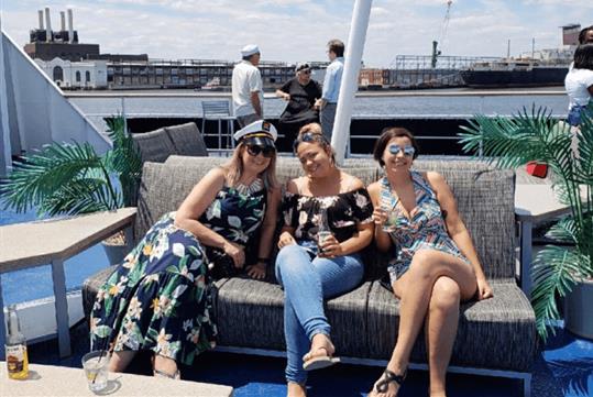 Three women sitting on an outdoor sofa smiling and posing for a photo on a sunny day on the Spirit of Philadelphia Signature Lunch Cruise.
