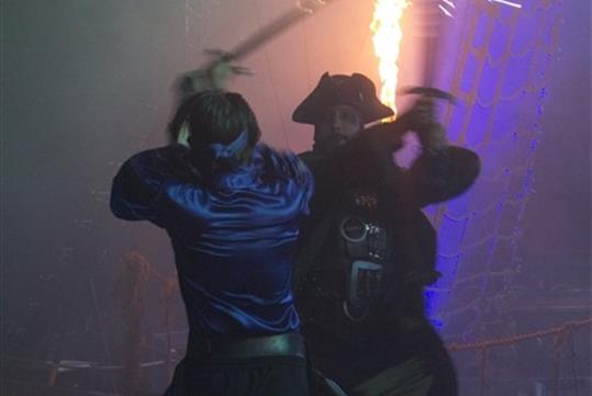Two pirates sword fighting on a dark ship with a bright fire behind them at Pirates Dinner Adventure Orlando.