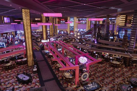 View looking down on the Planet Hollywood Casino with pink lighting and several different seating areas and game tables.