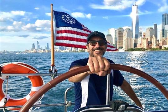 The captain at the wheel of a Private Sailboat Charter to the Statue of Liberty and NYC.