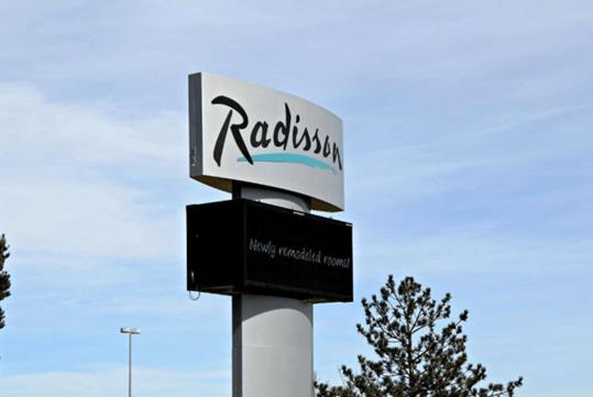 The silver and black sign for the Radisson Hotel Denver Central  with a tree next to it and a blue sky behind it.