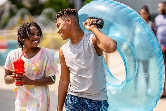 Two teenagers having a good time at Raging Waters Los Angeles, one wearing a tie dye swim cover up and the other holding a blue inner tube.