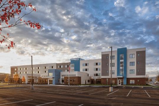 Wide shot of the blue, white, and gray front exterior of the Residence Inn by Marriott Columbus Airport with the sunset shining on it.