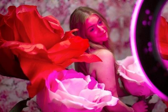Girl posing with giant pink and red flowers with a purple ring light pointed at her at Ripley's Selfie Studio.