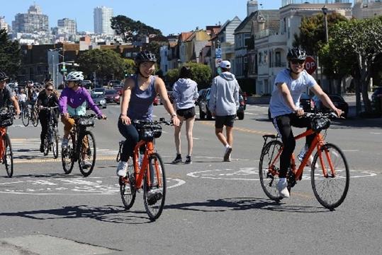 Tourists wearing helmets and riding bikes down a paved street with houses behind them on a sunny day in San Diego, California.