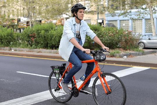 A man wearing a light blue jacket, jeans, and a black helmet while riding a red-orange bicycle down the street in Santa Monica.