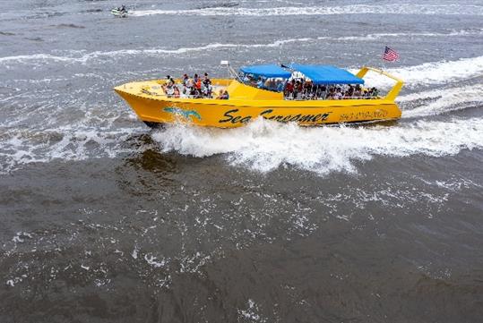 Aerial view looking down on the bright yellow Sea Screamer speed boat with its deck full of people.