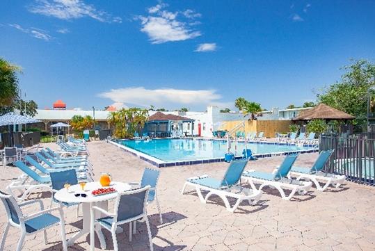 A large outdoor swimming pool with lounge chairs and tables around it on a sunny day at the Seralago Hotel & Suites Main Gate East.
