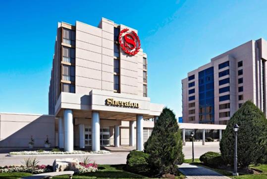 The front exterior of the Sheraton Parkway Toronto North Hotel & Suites with elegant landscaping on a sunny day.