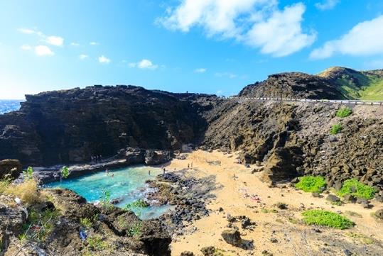 Aerial view looking over Halona Beach Cove at the Halona Blowhole Lookout with people playing in the water on sunny day.