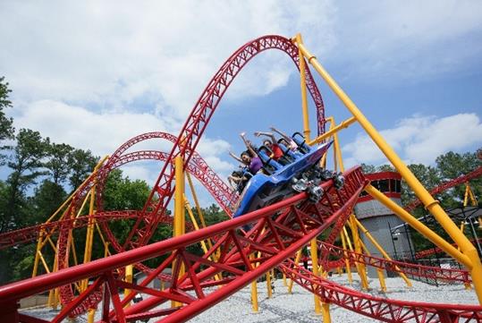 Guests having a good time riding the red and yellow Dare Devil Dive coaster with their arms up on a sunny day at Six Flags.