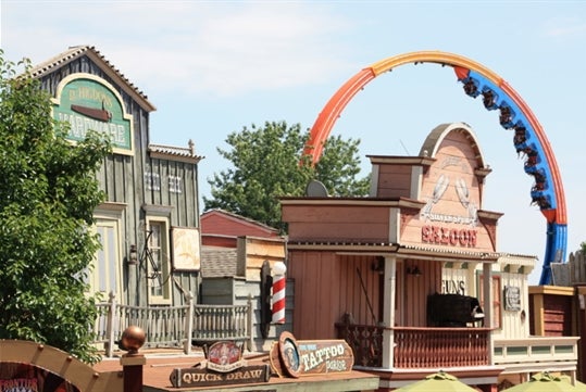 The main street of Frontier City features a barber shop, saloon, and parlor, with the Brain Drain roller coaster ride located behind it at Six Flags Frontier City.