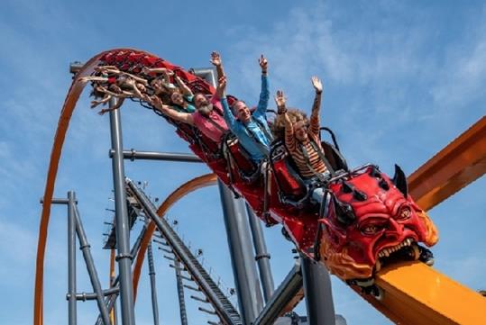 Guests with their hands up riding the red and orange Jersey Devil coaster on a sunny day.