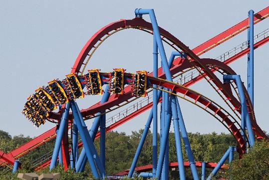 Park guests flying through the air on the Superman ride designed with striking blue frames and bold red tracks with trees in the background at Six Flags Great America.