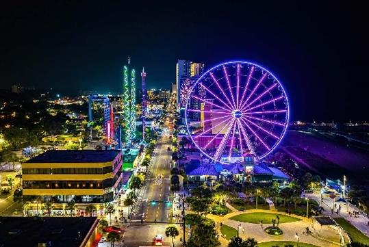 Aerial view of the Myrtle Beach SkyWheel glowing bright purple on a dark night with other city lights around it.