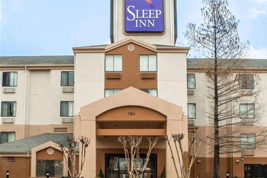 The front exterior of the Sleep Inn Arlington Near Six Flags with dead trees and shrubs in the landscaping.