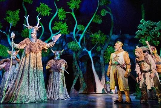 The cast of Spamalot performing on stage with dimly lit fake trees in the background in New York City, New York.