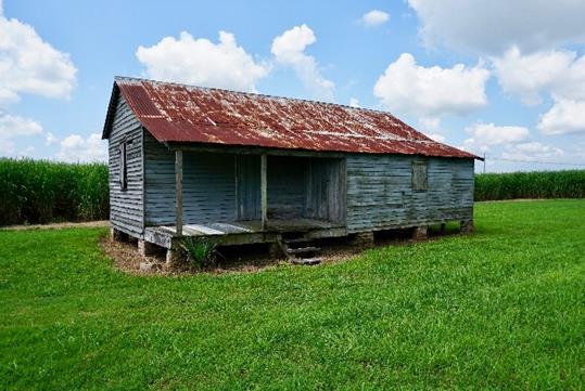 An old worn building with wooden slat walls, and a rusted tin roof on a sunny day at the Felicity Plantation in Vacherie, LA