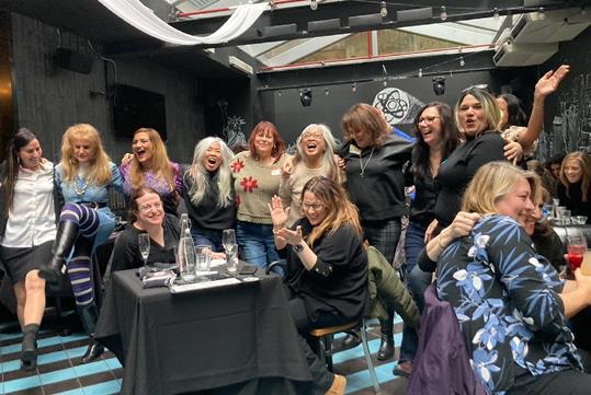 A line of women with their arms around each other dancing and having a good time at the Dueling Pianos Boozy Brunch.