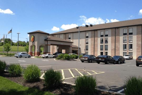 View of the front exterior of the Super 8 by Wyndham Mount Laurel with several cars in the parking lot and a blue cloudy sky overhead.