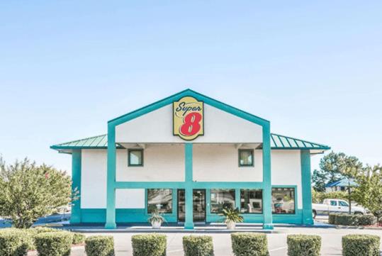 The front entrance of the Super 8 by Wyndham Valdosta/Conf Center Area, a white building with turquoise trim and roof on a bright sunny day.