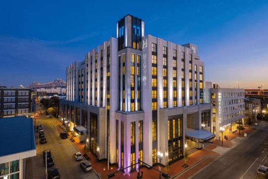 Wide shot of the two sides of the exterior of the The Higgins Hotel New Orleans at dusk with the street lights below on.