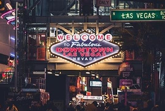 An iconic "Welcome to the Fabulous Downtown Las Vegas Nevada" sign at night with lights illuminating it and a crowd of people below it.