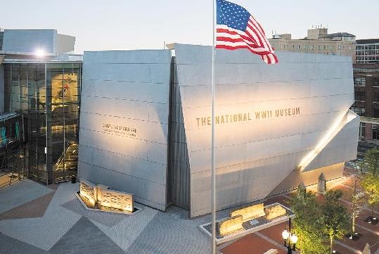 The exterior of the National WWII Museum with small trees on the right and an American flag flying high in New Orleans.