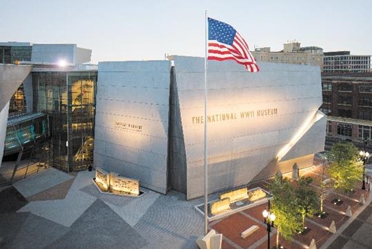 The exterior of the National WWII Museum with small trees on the right and an American flag flying high in New Orleans.