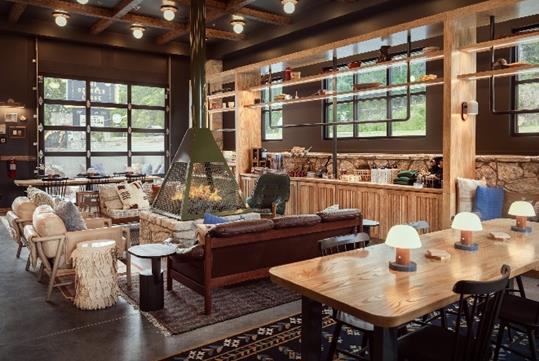 A lobby lounge area with rustic decor and plenty of seating around an indoor fire pit with large paneled windows all around the room.