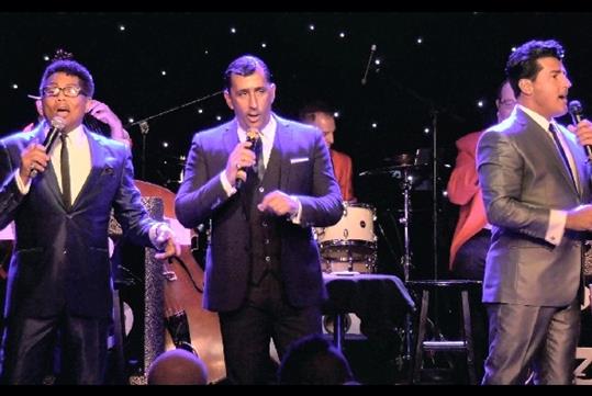 Three men in suits sining into microphones with a full band behind them on stage at the The Rat Pack is Back! show in Las Vegas.