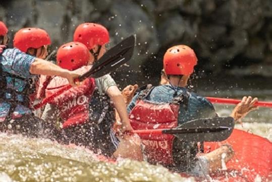 A group of people in red helmets splashing into the water at Smoky Mountain Rafting on the Upper Pigeon River.